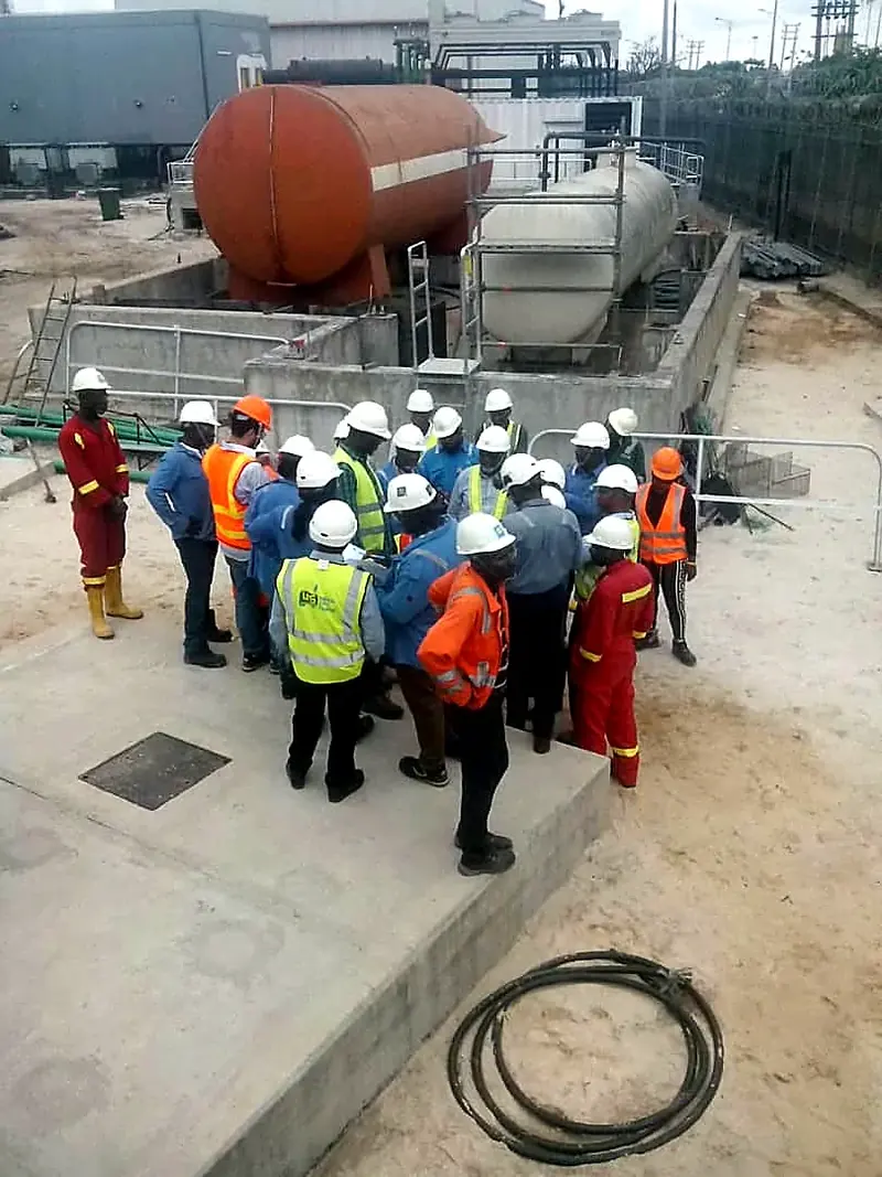 Site personnel in safety gear gathered for a briefing beside a tank