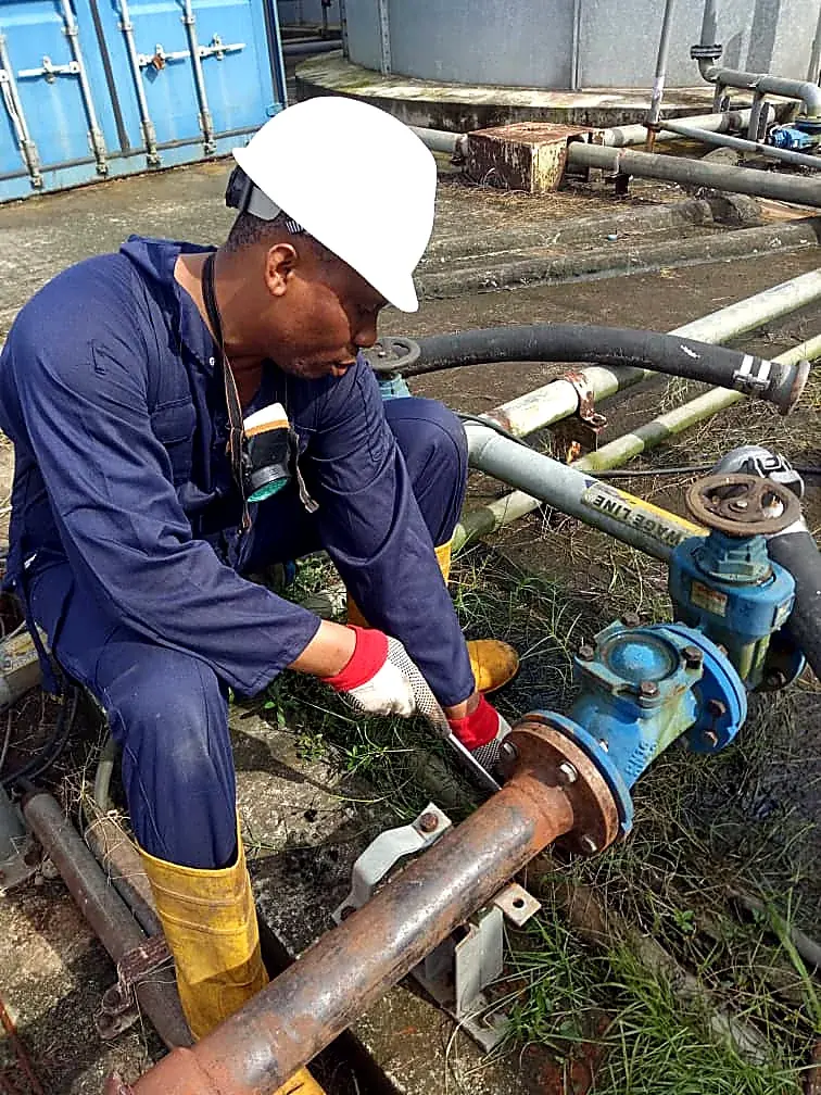 Technician in a hard hat and gloves working on a blue valve and pipework