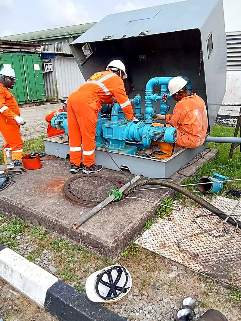 Technicians in orange overalls working on a pump unit at an equipment enclosure