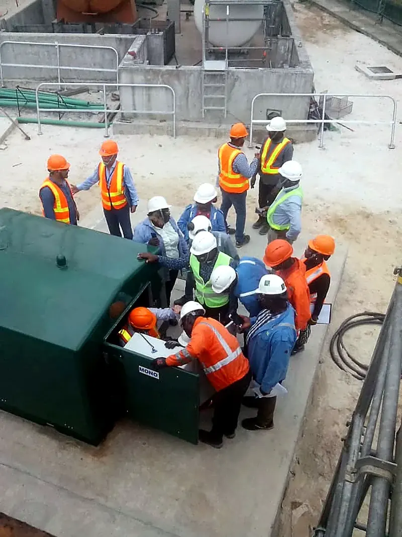 Personnel in safety gear gathered around a green tank at a treatment site