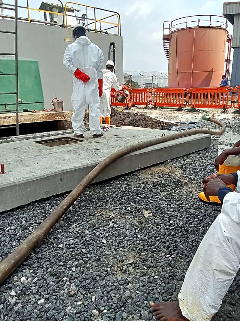 Technician in a white protective suit handling a hose at a treatment area